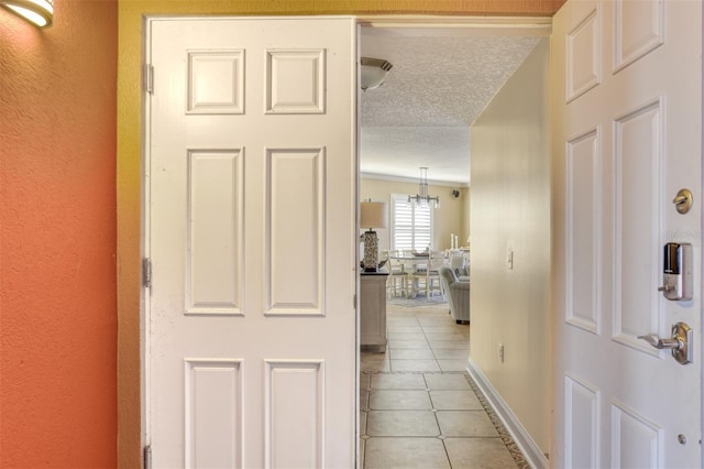 hallway with a textured ceiling, baseboards, and light tile patterned floors