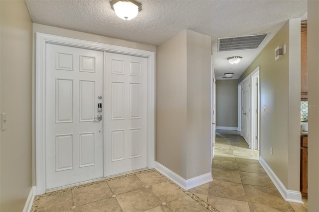 foyer with light tile patterned floors, a textured ceiling, visible vents, and baseboards