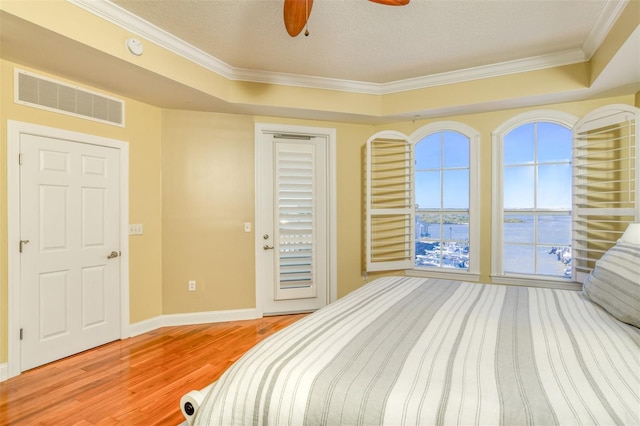 bedroom with visible vents, baseboards, light wood-type flooring, a tray ceiling, and crown molding