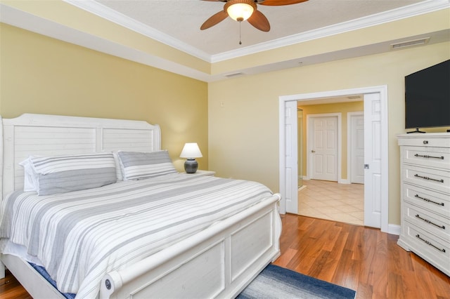 bedroom with ornamental molding, visible vents, light wood finished floors, and a ceiling fan