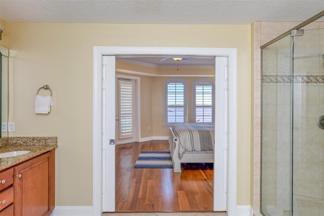 ensuite bathroom featuring a textured ceiling, wood finished floors, a shower stall, and baseboards