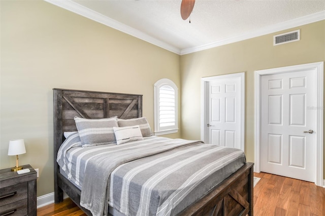 bedroom featuring wood finished floors, visible vents, and crown molding