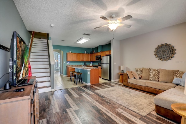 living area with arched walkways, visible vents, light wood-style flooring, stairway, and a textured ceiling