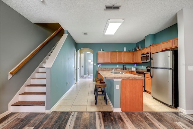 kitchen with arched walkways, a center island with sink, visible vents, appliances with stainless steel finishes, and a sink