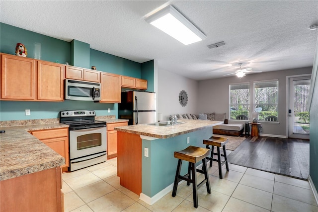 kitchen with stainless steel appliances, light countertops, light tile patterned flooring, and a kitchen bar