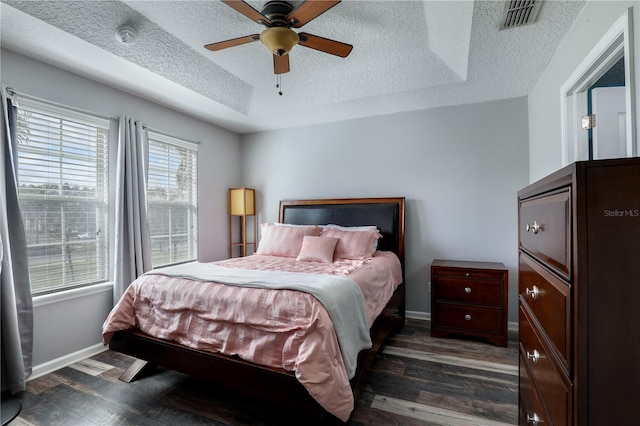 bedroom with a raised ceiling, visible vents, baseboards, and wood finished floors