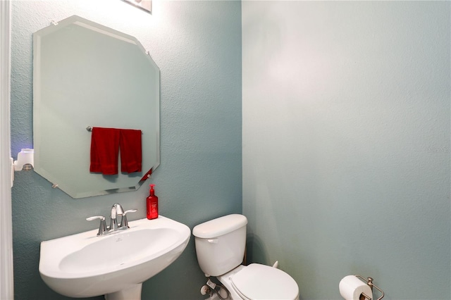 half bath with a textured wall, a sink, and toilet