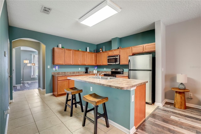 kitchen featuring arched walkways, stainless steel appliances, a sink, visible vents, and light countertops