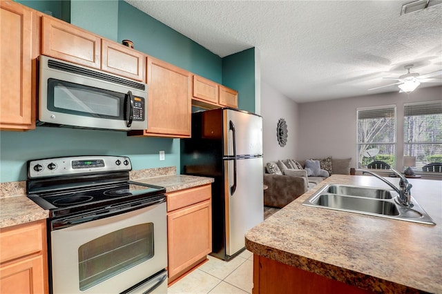 kitchen with a textured ceiling, light tile patterned flooring, light brown cabinets, stainless steel appliances, and a sink