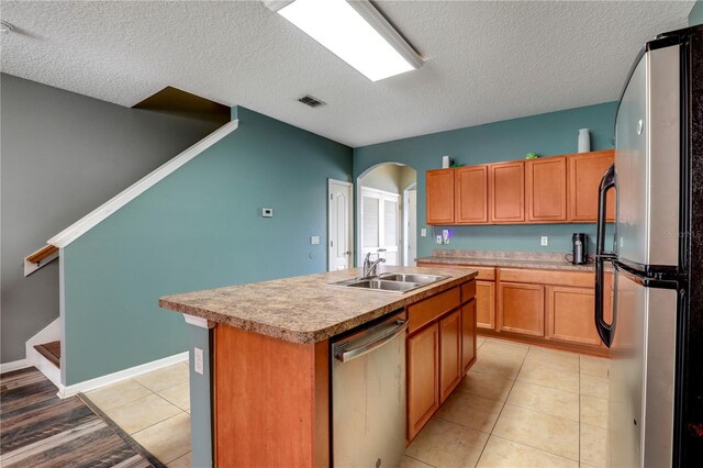 kitchen featuring arched walkways, a center island with sink, stainless steel appliances, visible vents, and a sink