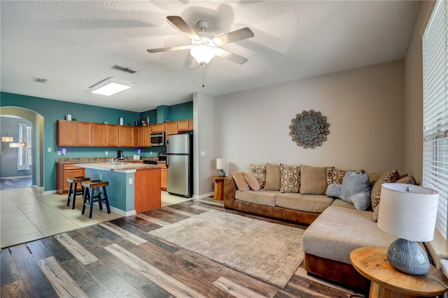 living area with arched walkways, ceiling fan, light wood-type flooring, and visible vents