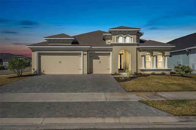 view of front facade with stucco siding, an attached garage, decorative driveway, and roof with shingles