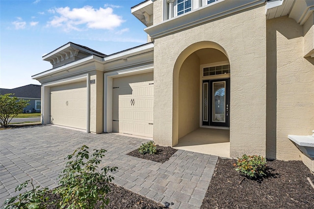 property entrance with stucco siding, decorative driveway, and an attached garage