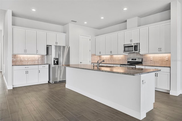 kitchen featuring visible vents, dark wood-type flooring, a center island with sink, appliances with stainless steel finishes, and white cabinets