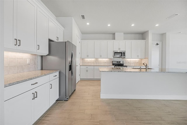 kitchen featuring light stone counters, stainless steel appliances, visible vents, and white cabinetry