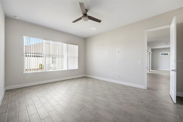 empty room featuring a ceiling fan, visible vents, wood finished floors, and baseboards