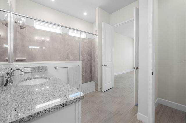 full bath with baseboards, a walk in shower, vanity, and wood finish floors