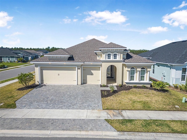 mediterranean / spanish-style home featuring a front yard, roof with shingles, stucco siding, decorative driveway, and a garage