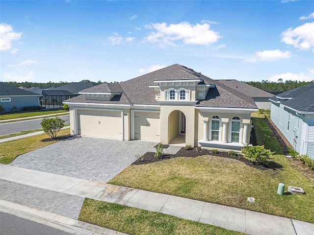 mediterranean / spanish-style house featuring roof with shingles, stucco siding, a front lawn, a garage, and decorative driveway