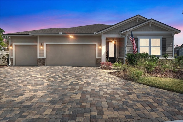 craftsman inspired home with an attached garage, stone siding, and decorative driveway