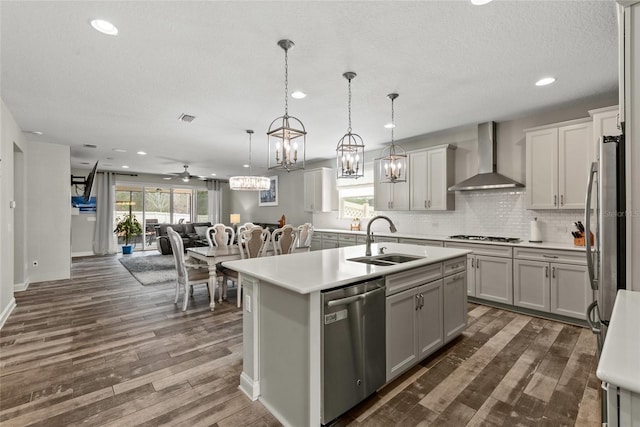 kitchen with stainless steel appliances, open floor plan, a sink, wall chimney range hood, and an island with sink