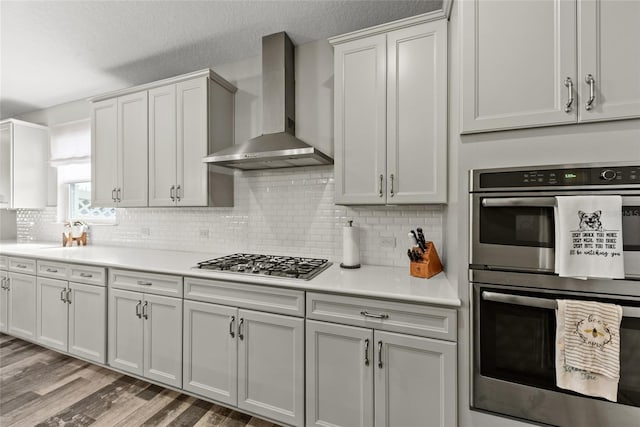 kitchen with light countertops, light wood-style flooring, decorative backsplash, appliances with stainless steel finishes, and wall chimney range hood