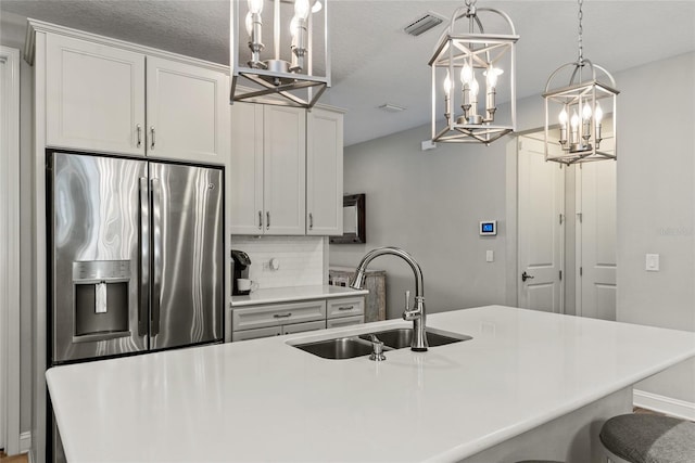 kitchen featuring stainless steel fridge, visible vents, light countertops, pendant lighting, and a sink