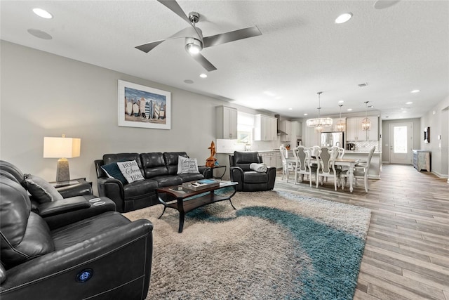 living room with light wood-style flooring, ceiling fan with notable chandelier, a textured ceiling, and recessed lighting