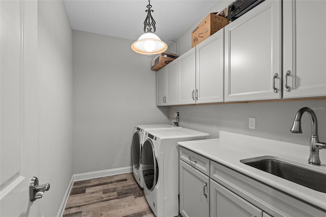 clothes washing area featuring separate washer and dryer, a sink, baseboards, cabinet space, and light wood finished floors