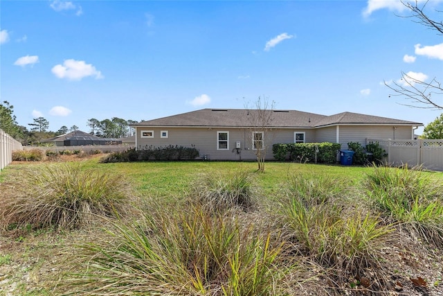 rear view of house featuring a lawn and fence