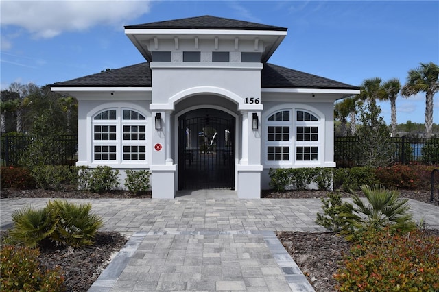 view of front facade with a shingled roof, fence, and stucco siding