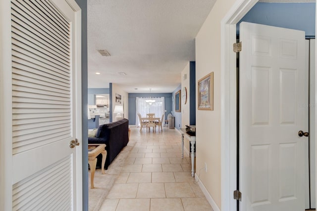 hallway with a textured ceiling, light tile patterned flooring, visible vents, baseboards, and an inviting chandelier