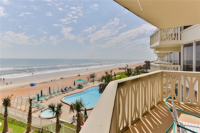 view of swimming pool with a water view, fence, and a view of the beach