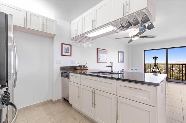 kitchen with stainless steel appliances, a peninsula, a sink, a ceiling fan, and dark stone countertops