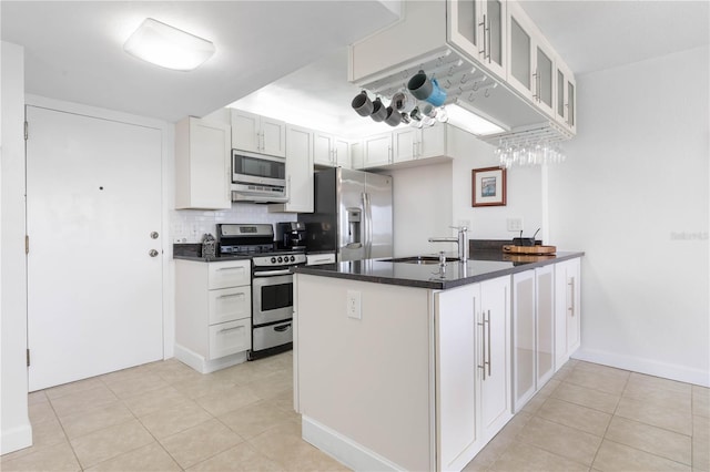 kitchen featuring dark countertops, appliances with stainless steel finishes, glass insert cabinets, a peninsula, and a sink