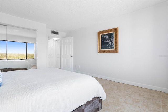 bedroom featuring baseboards, visible vents, a textured ceiling, a closet, and light tile patterned flooring