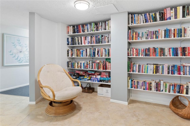 sitting room featuring a textured ceiling, wall of books, tile patterned flooring, and baseboards