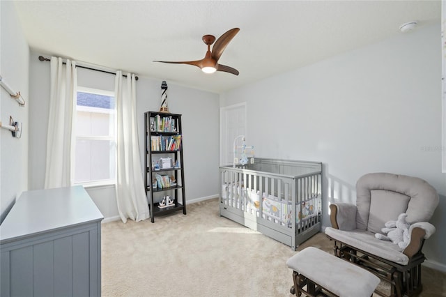 bedroom featuring light carpet, a nursery area, ceiling fan, and baseboards