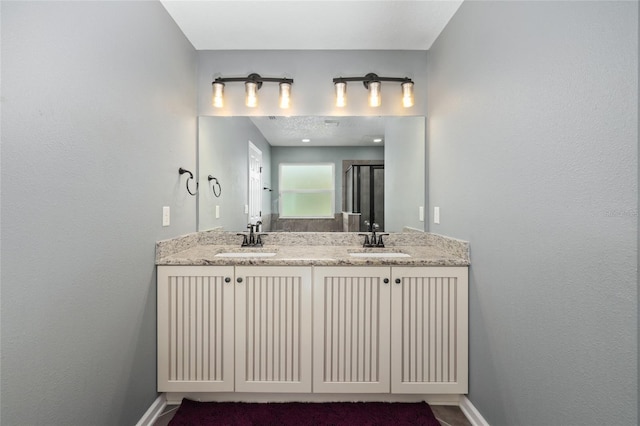 full bath featuring a sink, baseboards, a stall shower, and double vanity