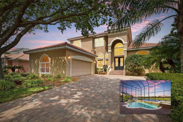 mediterranean / spanish home with decorative driveway, an attached garage, a tile roof, stucco siding, and french doors