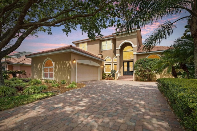 mediterranean / spanish house with french doors, stucco siding, a tiled roof, decorative driveway, and a garage