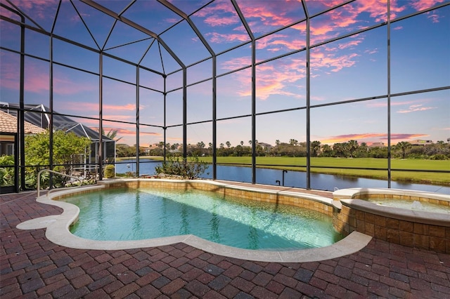 pool at dusk featuring a water view, a pool with connected hot tub, a lanai, and a patio area