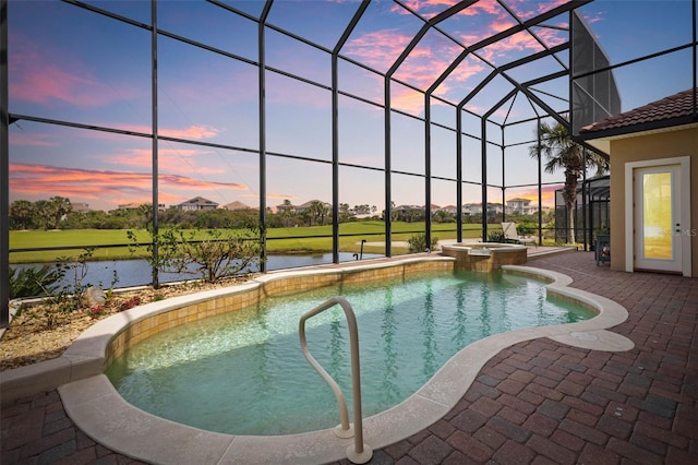 pool at dusk with a pool with connected hot tub, a water view, glass enclosure, and a patio area