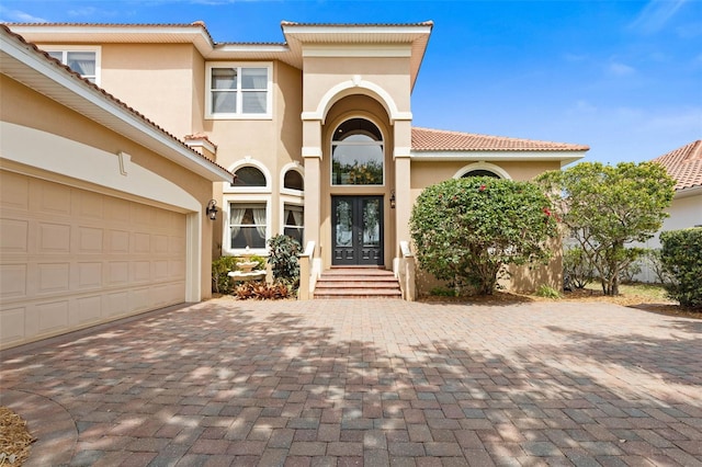 mediterranean / spanish house featuring a tile roof, french doors, stucco siding, decorative driveway, and a garage