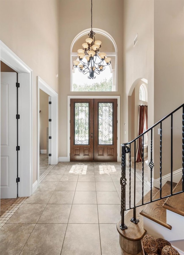 entryway featuring a chandelier, stairs, a towering ceiling, french doors, and light tile patterned floors
