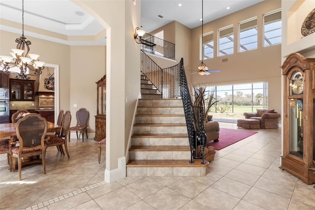 staircase featuring baseboards, a towering ceiling, arched walkways, ceiling fan with notable chandelier, and tile patterned flooring