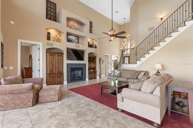 tiled living area with stairway, a ceiling fan, built in shelves, a glass covered fireplace, and visible vents