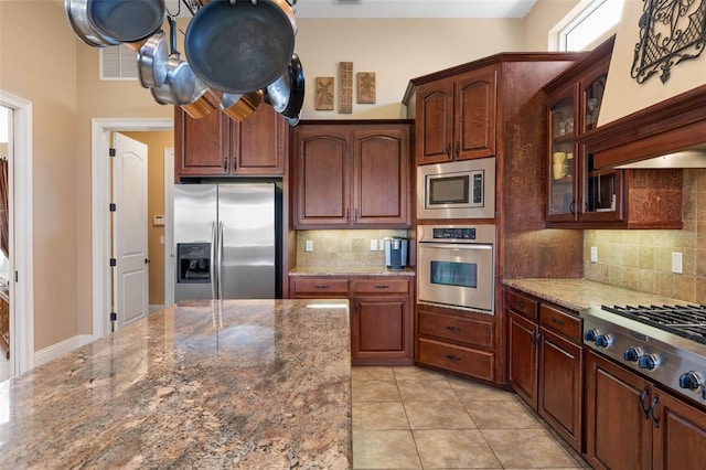 kitchen with glass insert cabinets, dark stone counters, tasteful backsplash, and stainless steel appliances