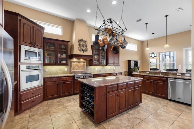 kitchen featuring backsplash, stone countertops, appliances with stainless steel finishes, premium range hood, and visible vents