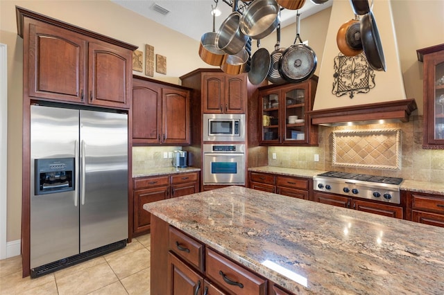kitchen with stainless steel appliances, backsplash, visible vents, light stone countertops, and glass insert cabinets